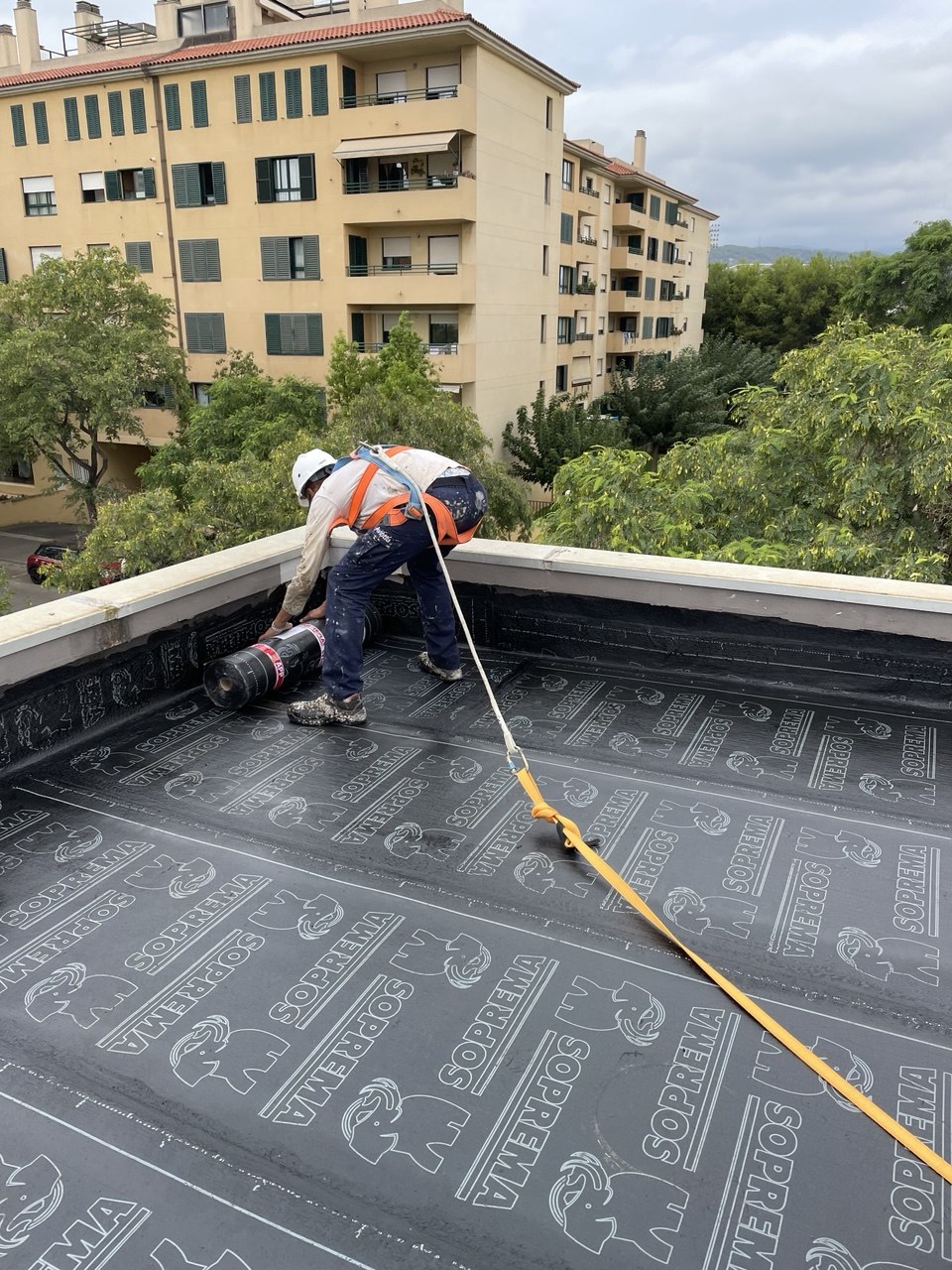 Operario aplicando membrana con arnés de seguridad